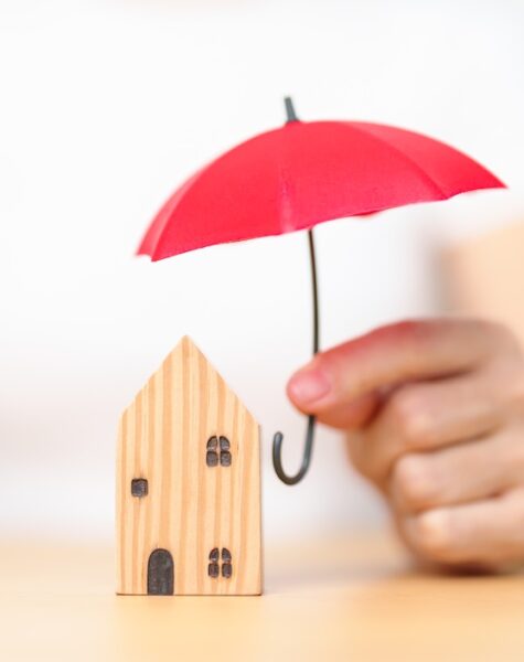 Businesswoman hand holding red Umbrella cover wooden Home model. real estate, insurance and property concepts Businesswoman hand holding red Umbrella cover wooden Home model. real estate, insurance and property concepts