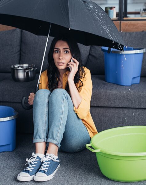 Confused woman with smartphone sitting under umbrella in living room Confused woman with smartphone sitting under umbrella in living room