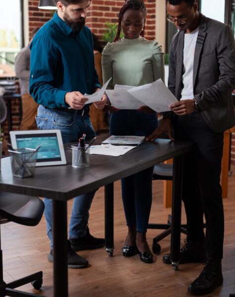 Diverse team holding papers analyzing marketing graph Diverse team holding papers analyzing marketing graph discussing business project in brick wall office. Multi-ethnic businesspeople brainstorming ideas working at company strategy. Corporate staff