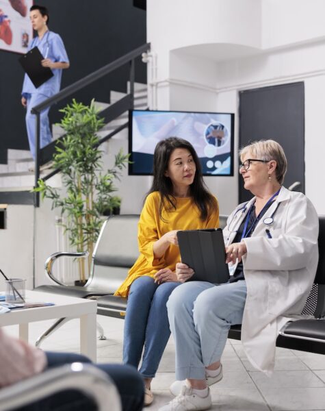 Old physician consulting asian patient at health center Old physician consulting asian patient at health center, analyzing disease report using digital tablet. Senior doctor talking to person with disease diagnosis at consultation in hospital waiting room