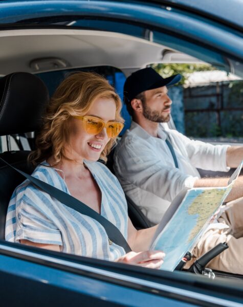 selective focus of cheerful woman holding map while man driving car selective focus of cheerful woman holding map while man driving car