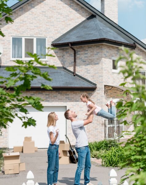 side view of father raising up daughter while mother standing near in front of their new house side view of father raising up daughter while mother standing near in front of their new house